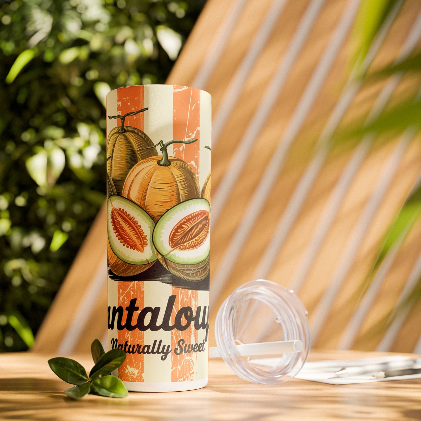 Retro Cantaloupe Skinny Tumbler with Straw placed on a wooden table surrounded by greenery, showcasing its stylish design for outdoor adventures.