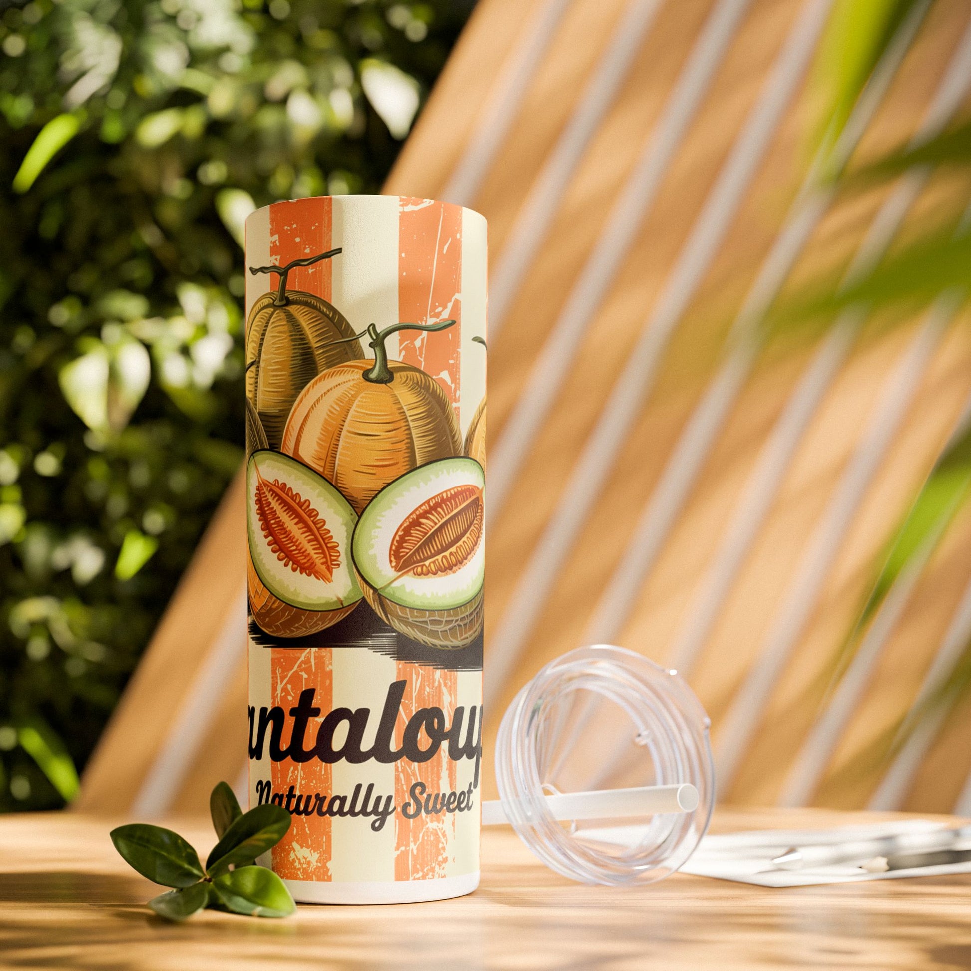 Retro Cantaloupe Skinny Tumbler with Straw placed on a wooden table surrounded by greenery, showcasing its stylish design for outdoor adventures.