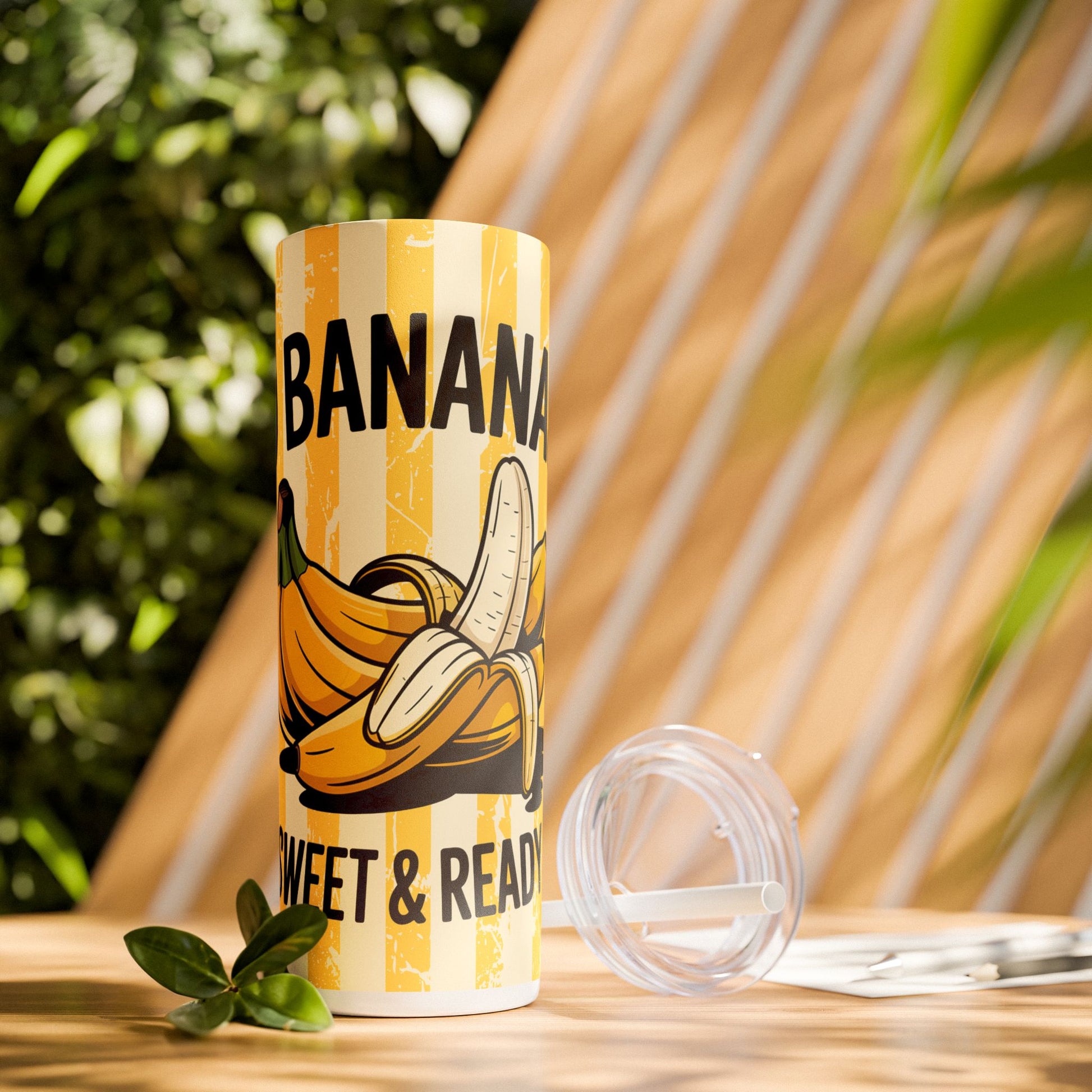 Stylish outdoor display of the Banana Lover's Eco-Friendly Drinkware 20oz Skinny Tumbler surrounded by greenery, ready for smoothies and juices.