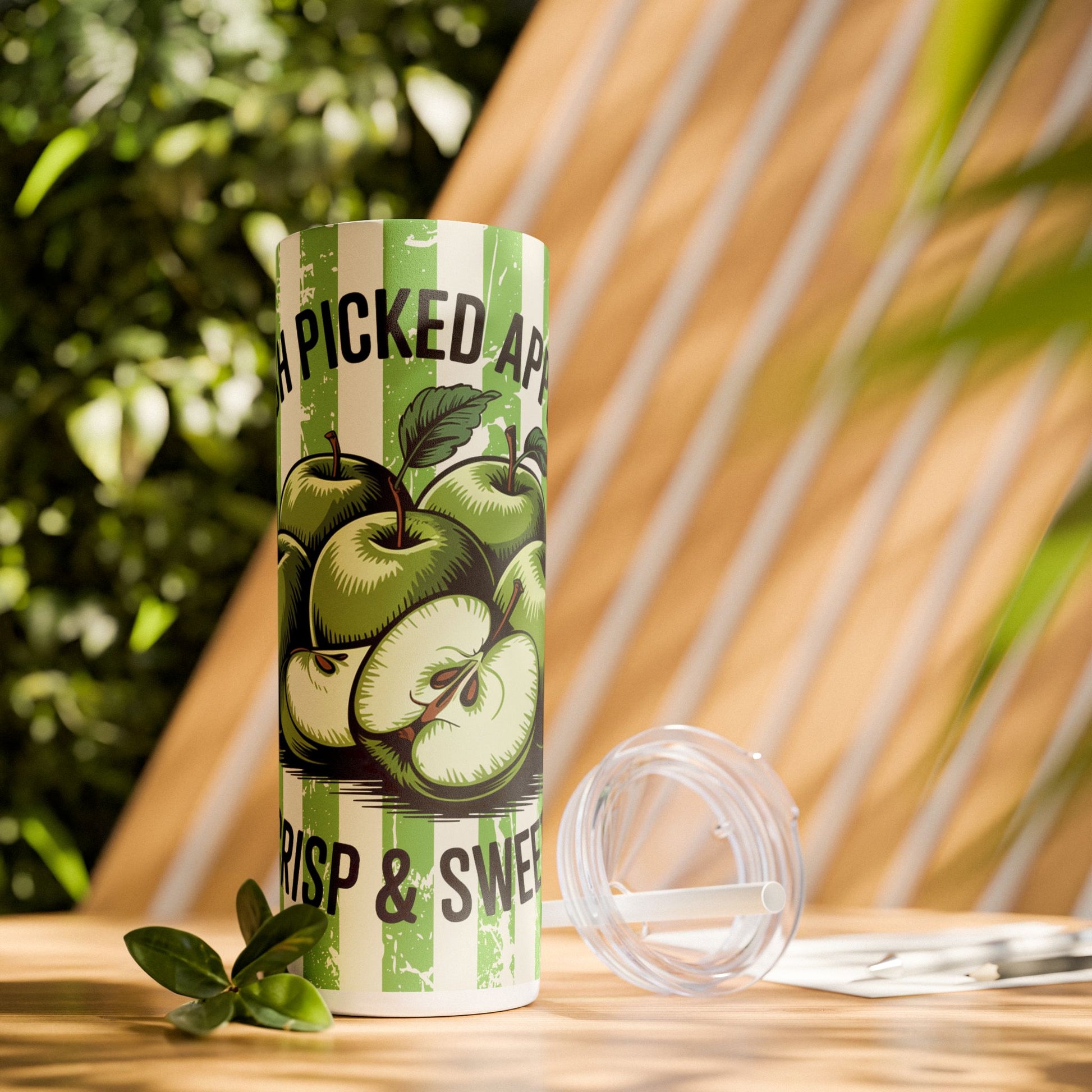 Lifestyle shot of a 20oz stainless steel tumbler with Crisp Apple design amidst greenery, showcasing its stylish look and practical features for hydration.